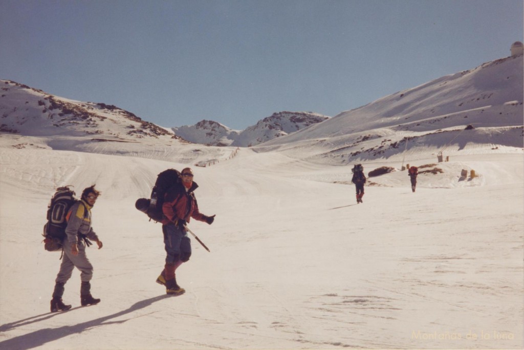 Delante Julio y Miguel Ángel cruzando las pistas de esquí con los Tajos de La Virgen al fondo y el observatorio arriba a la derecha